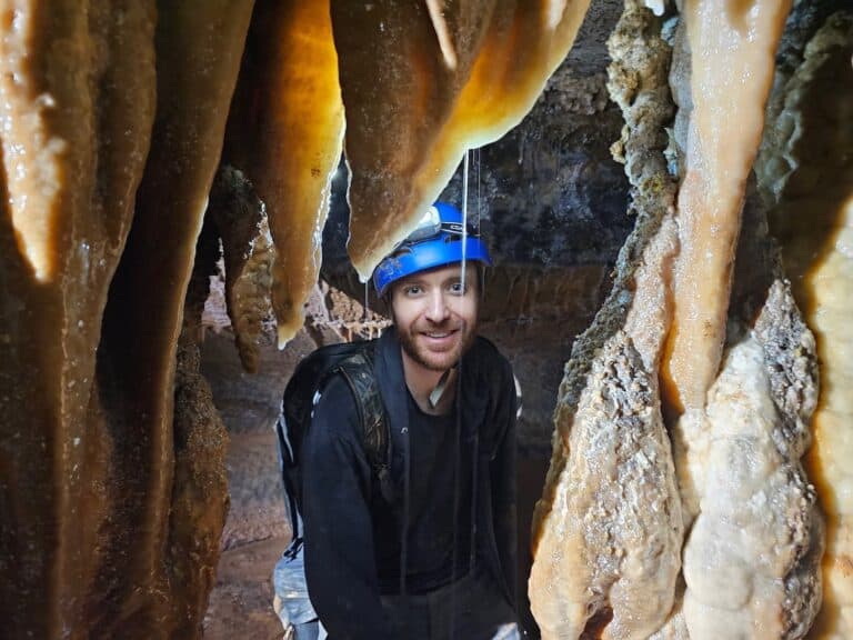 Mike smiling for a photo in a cave while being surrounded by cave formations